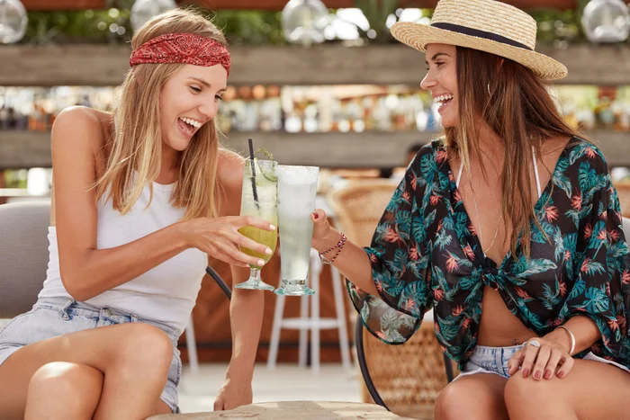 Beautiful overjoyed young females have summer party together, clink glass of cocktails, enjoy good recreation, have pleasant talk. cheerful best friends drink summer beverages. time to relax